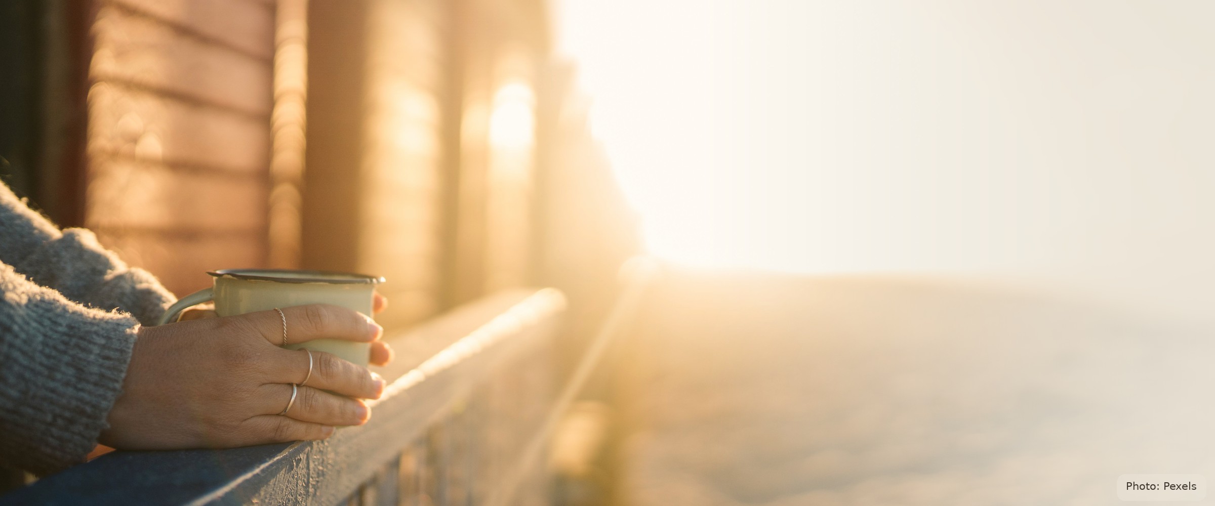 A hand wrapped around a warm mug rests on a porch railing at sunrise - steadiness, not the crisis.