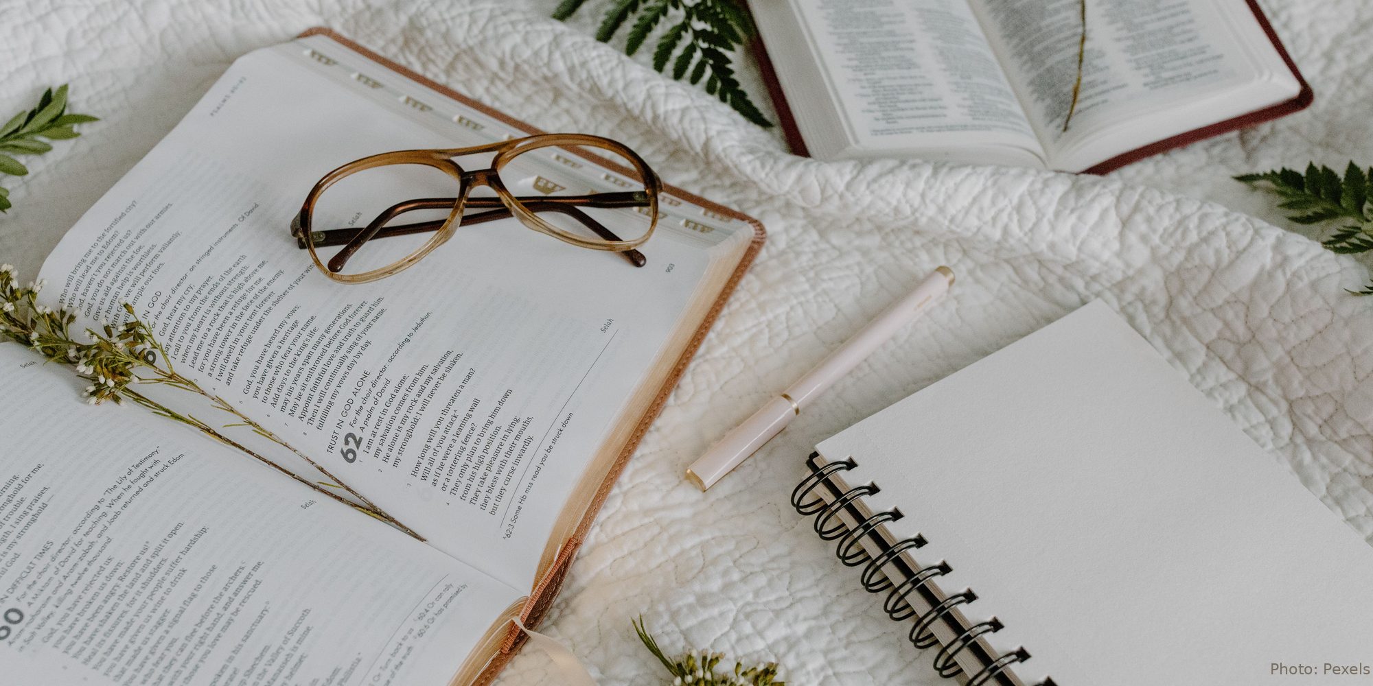 An open Bible rests on a white quilt at Psalm 62 - Trust in God Alone - beside reading glasses and a journal.