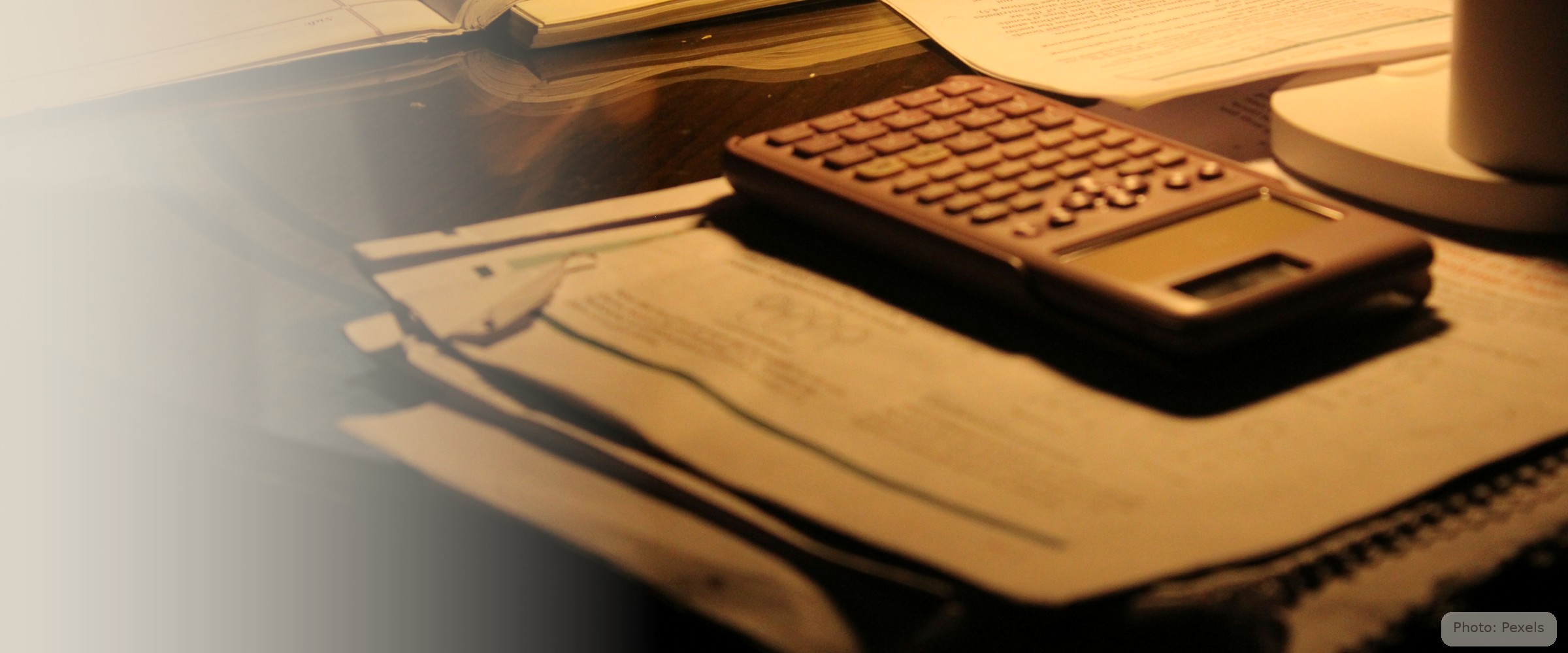 A calculator and papers sit under a single lamp on a table at night - the quiet math of a rent that no longer fits.