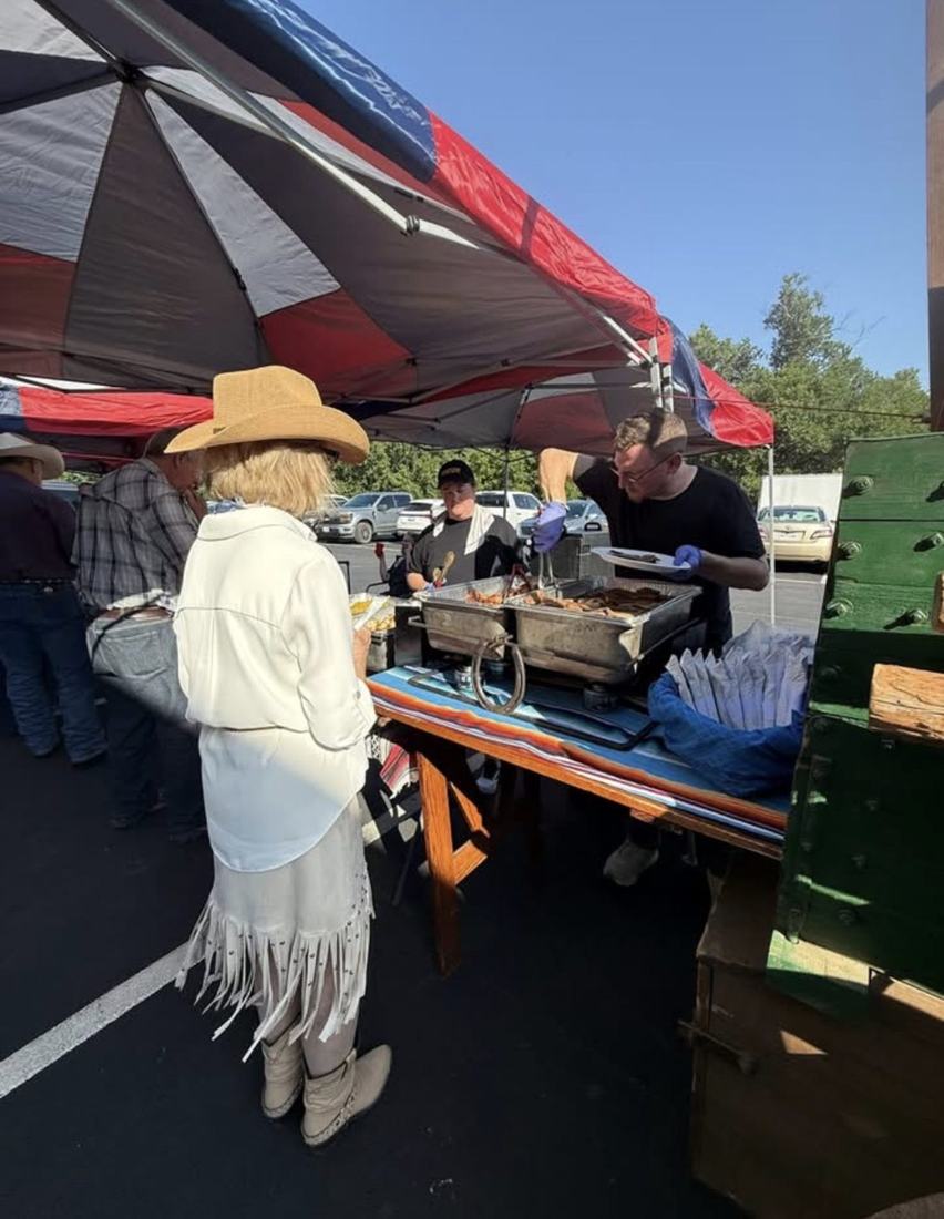 A guest is served barbecue from chafing dishes under a tent in the parking lot.