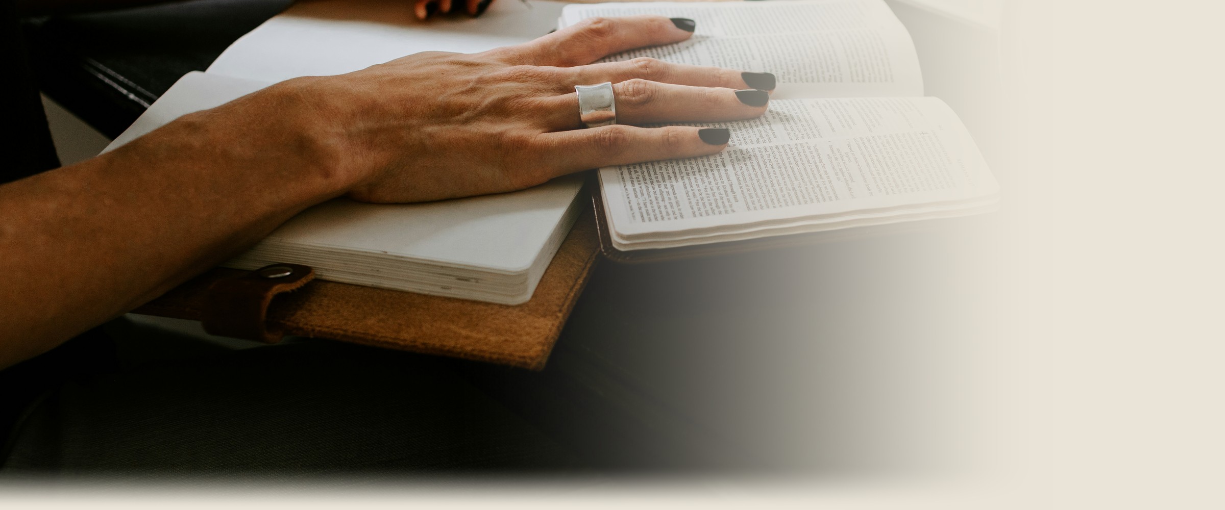 A woman's hands rest on an open Bible and journal at a sunlit table.