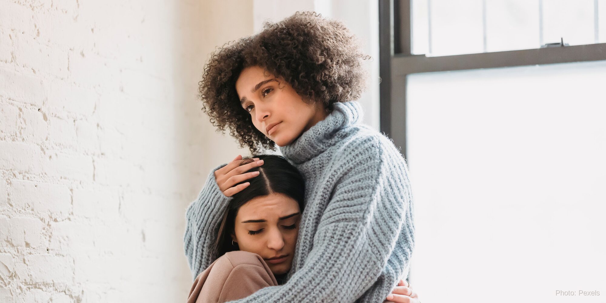 A woman rests her head on a friend's shoulder, met with a steady hand and no judgment - the opposite of hiding in shame.
