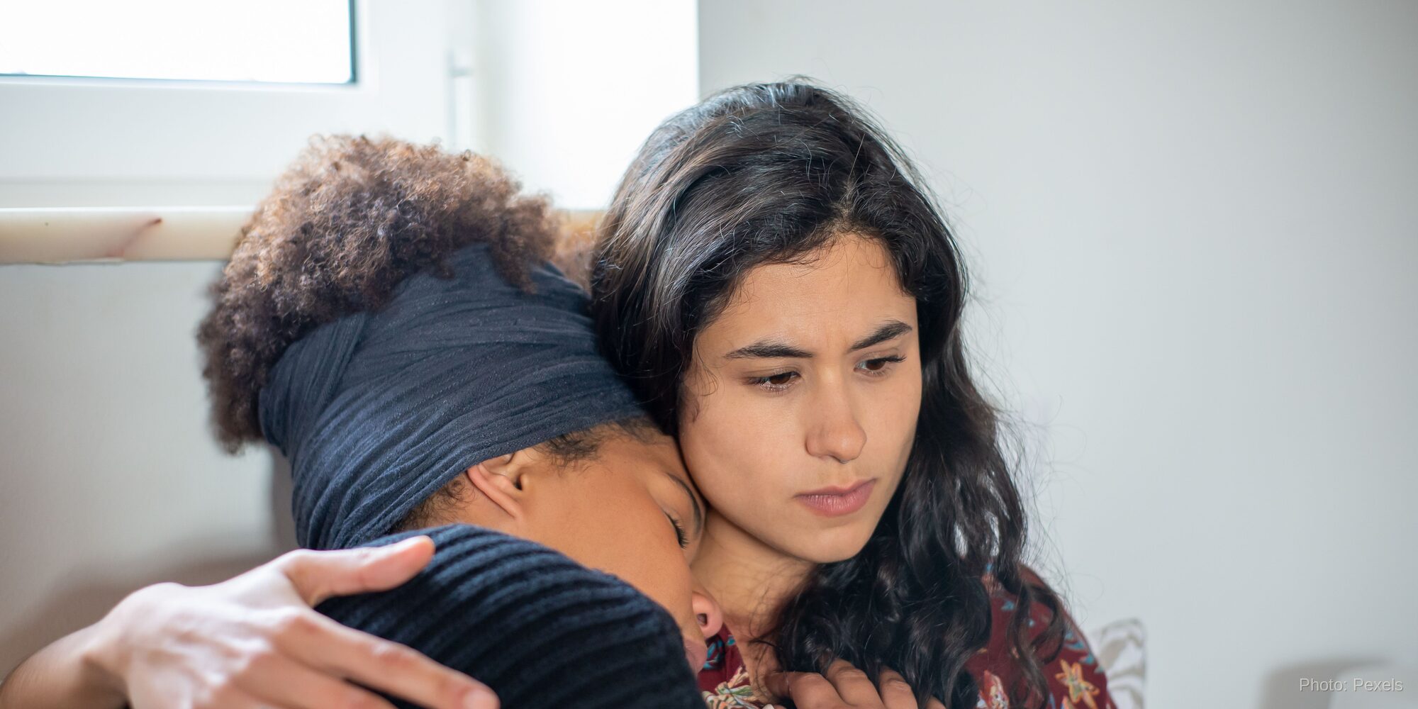 A woman rests safely in a friend's arms, met with quiet, steady attention - presence that says, I'm not going anywhere.